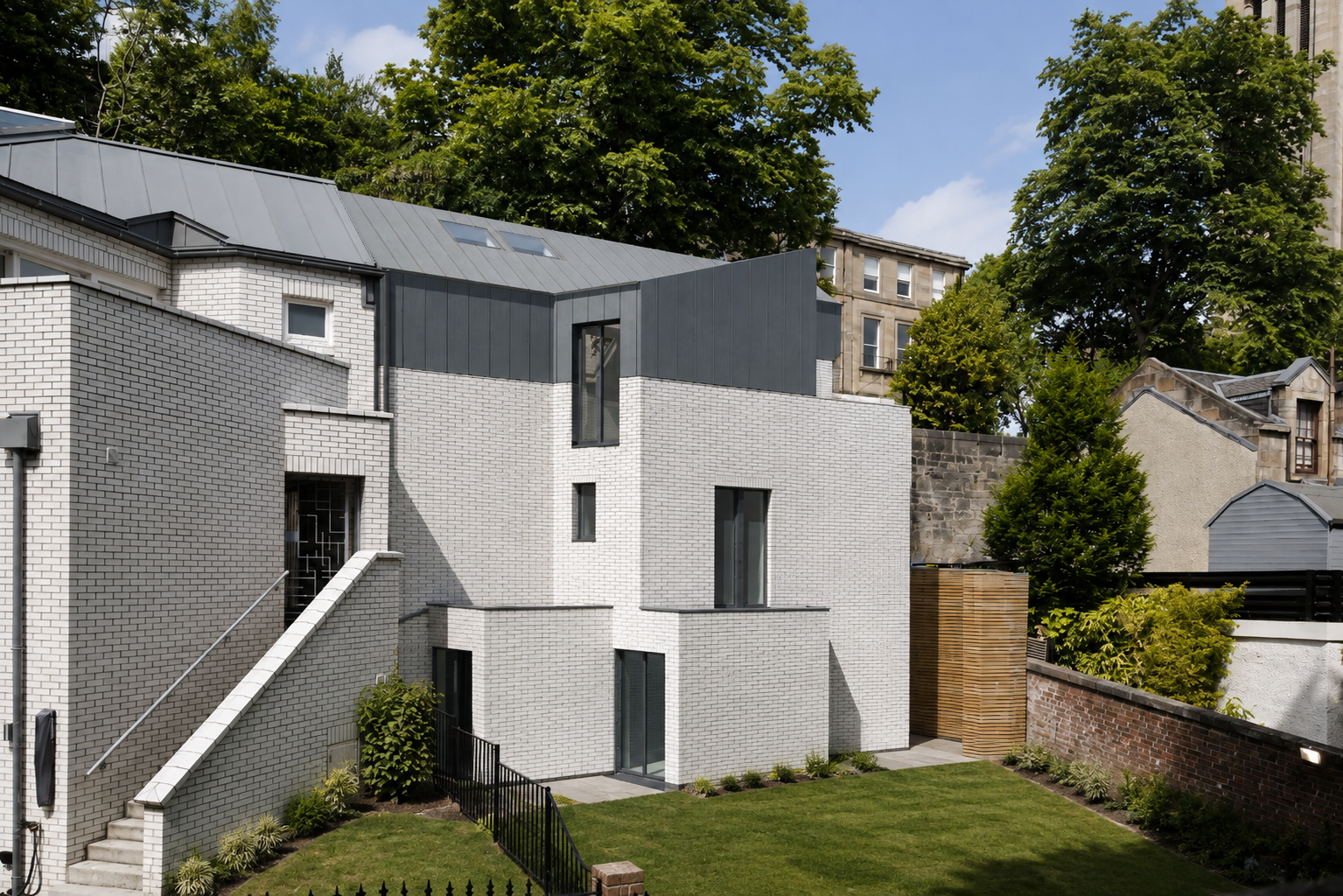 Landscaped garden courtyard beside a contemporary Glasgow mews house with pale brick walls, dark metal roof and mature surrounding trees