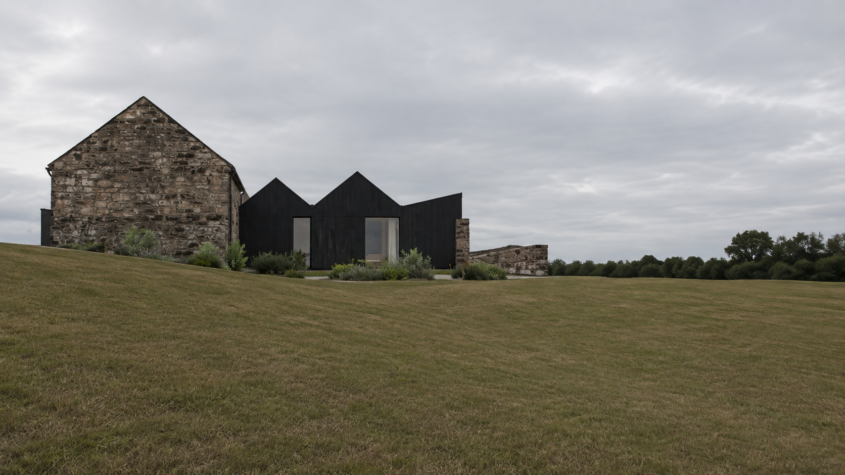 Traditional stone barn conversion in Helensburgh with a slate roof, narrow windows and contemporary black-clad extension.